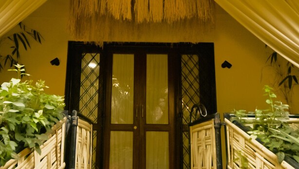 A room with a thatched roof entrance, wooden railings, and potted plants. - Angie's Gardenia a homestay for a comfortable experience  (Candolim)