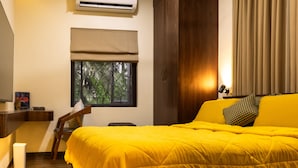 A hotel room with a bed, a desk, an air conditioner, a window with a view, and a curtain. - Angie's Gardenia a homestay for a comfortable experience  (Candolim)