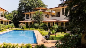 A pool surrounded by lush greenery and a building with multiple balconies. - Angie's Gardenia a homestay for a comfortable experience  (Candolim)