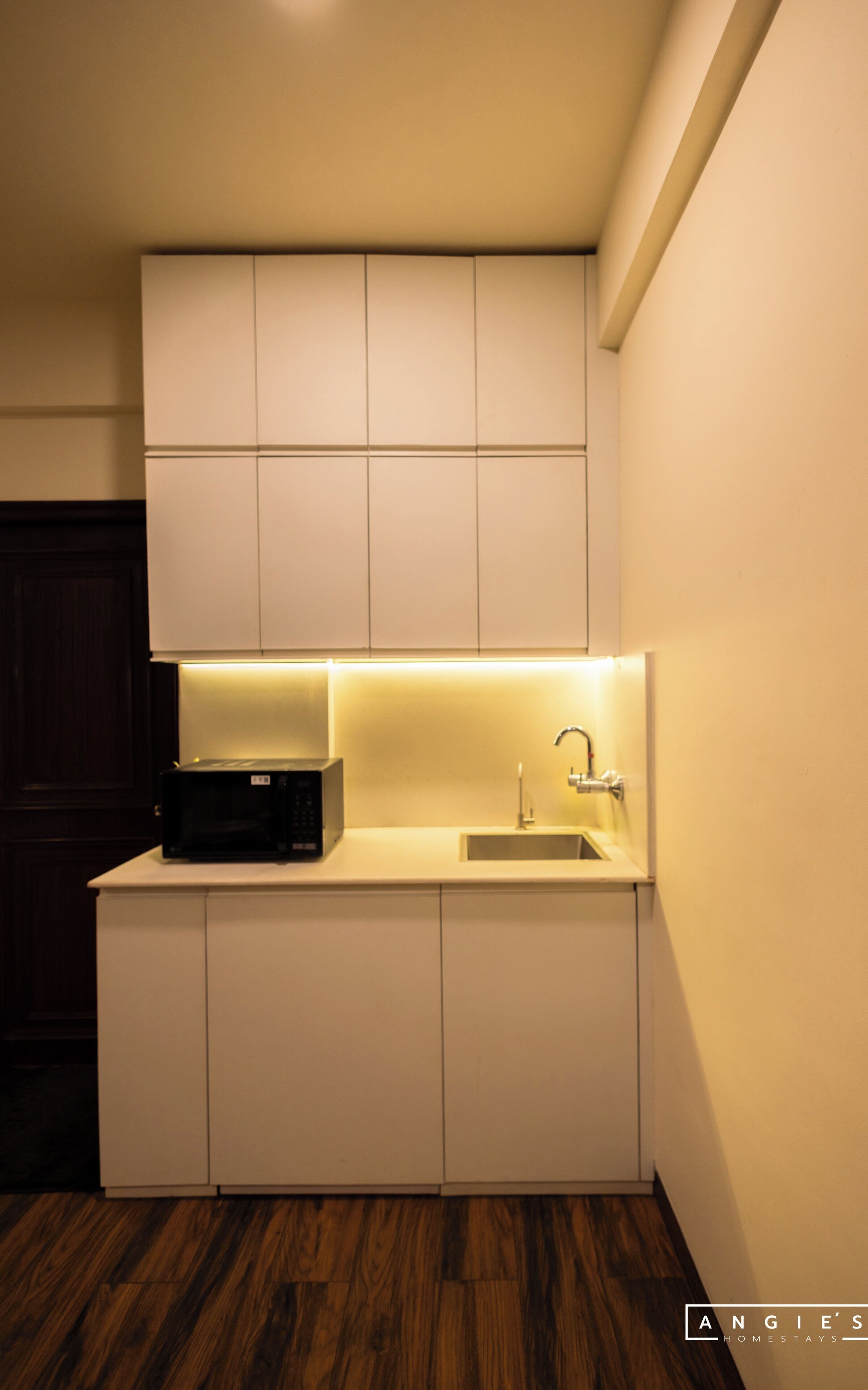 Une cuisine compacte équipée d’un four à micro-ondes encastré, d’un évier et d’un meuble de rangement au-dessus du plan de travail.
