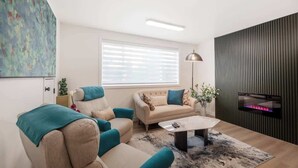 Ein modernes Wohnzimmer mit einem beigefarbenen Sofagarnitur, einem Couchtisch und einem großen Fenster mit Jalousien.