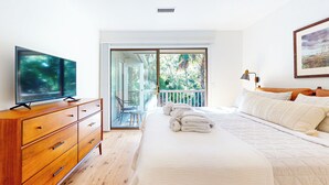 Un dormitorio con una cama grande, un aparador de madera, una televisión y un balcón con vistas a árboles.
