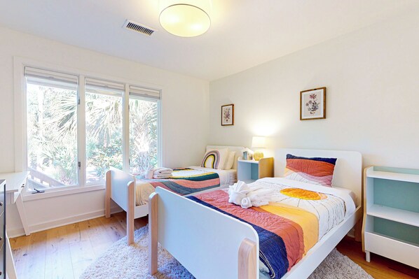 A bedroom with two beds, a desk, and a window with a view of trees.