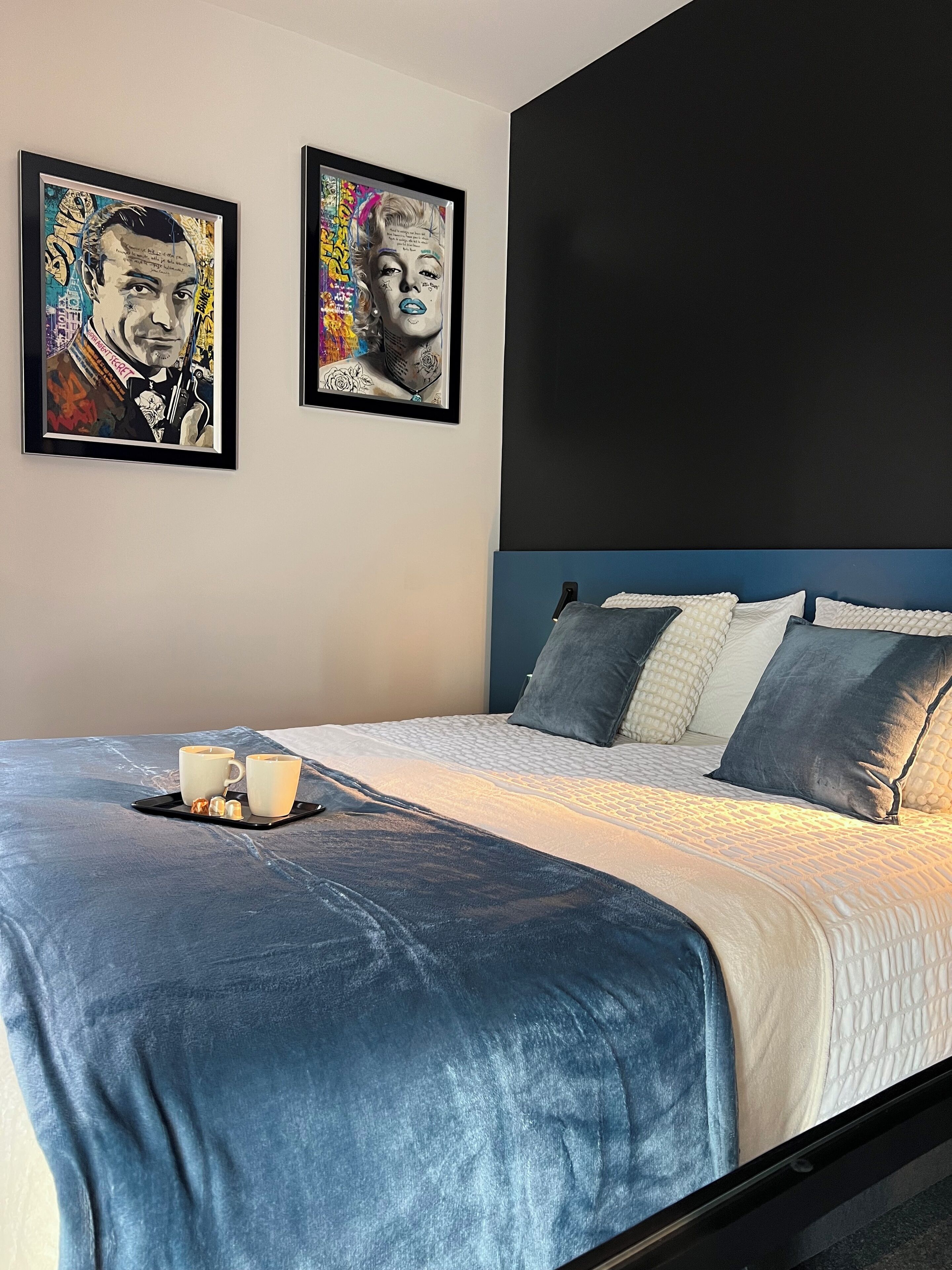 A bedroom with a bed, two framed artworks, and a tray with cups and snacks.
