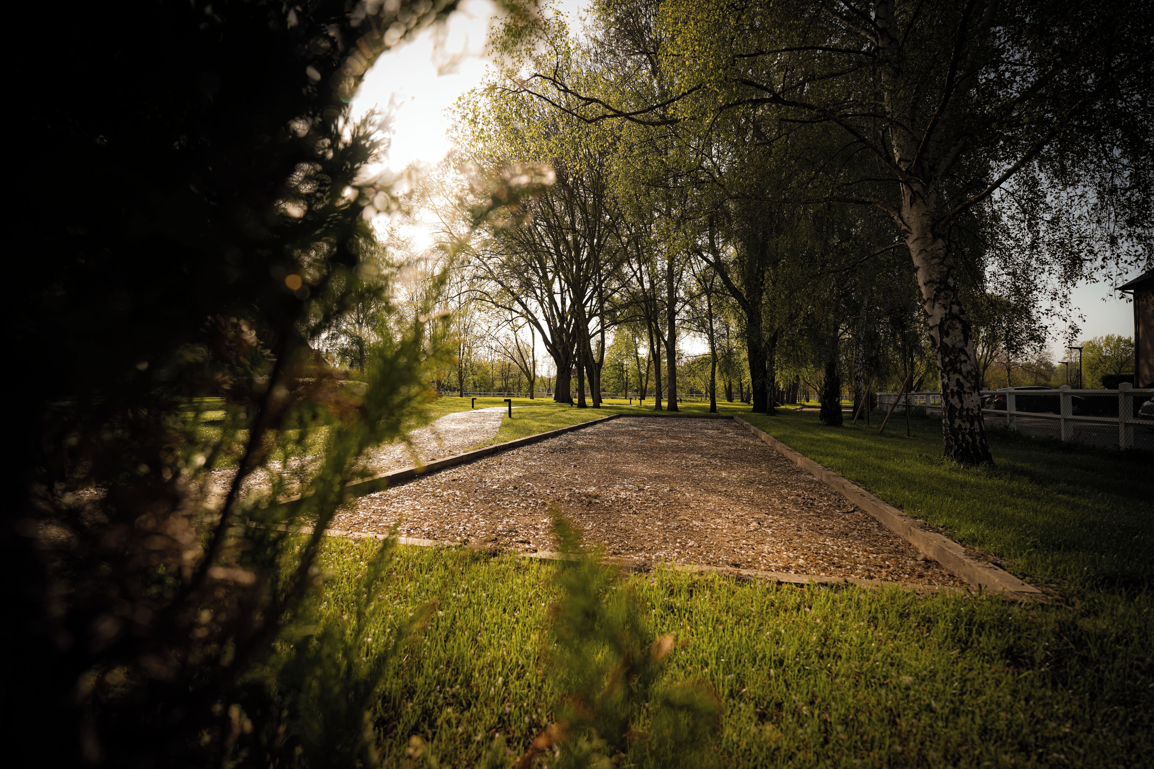 A park with a paved area, trees, and a white fence.