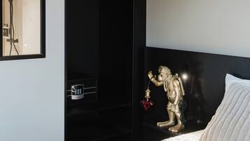 A modern hotel room with a bed, a black wardrobe, a gold statue, and a wall-mounted control panel.