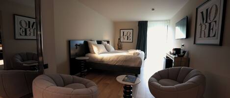 A modern bedroom with a bed, two armchairs, a small table, and artwork on the walls.