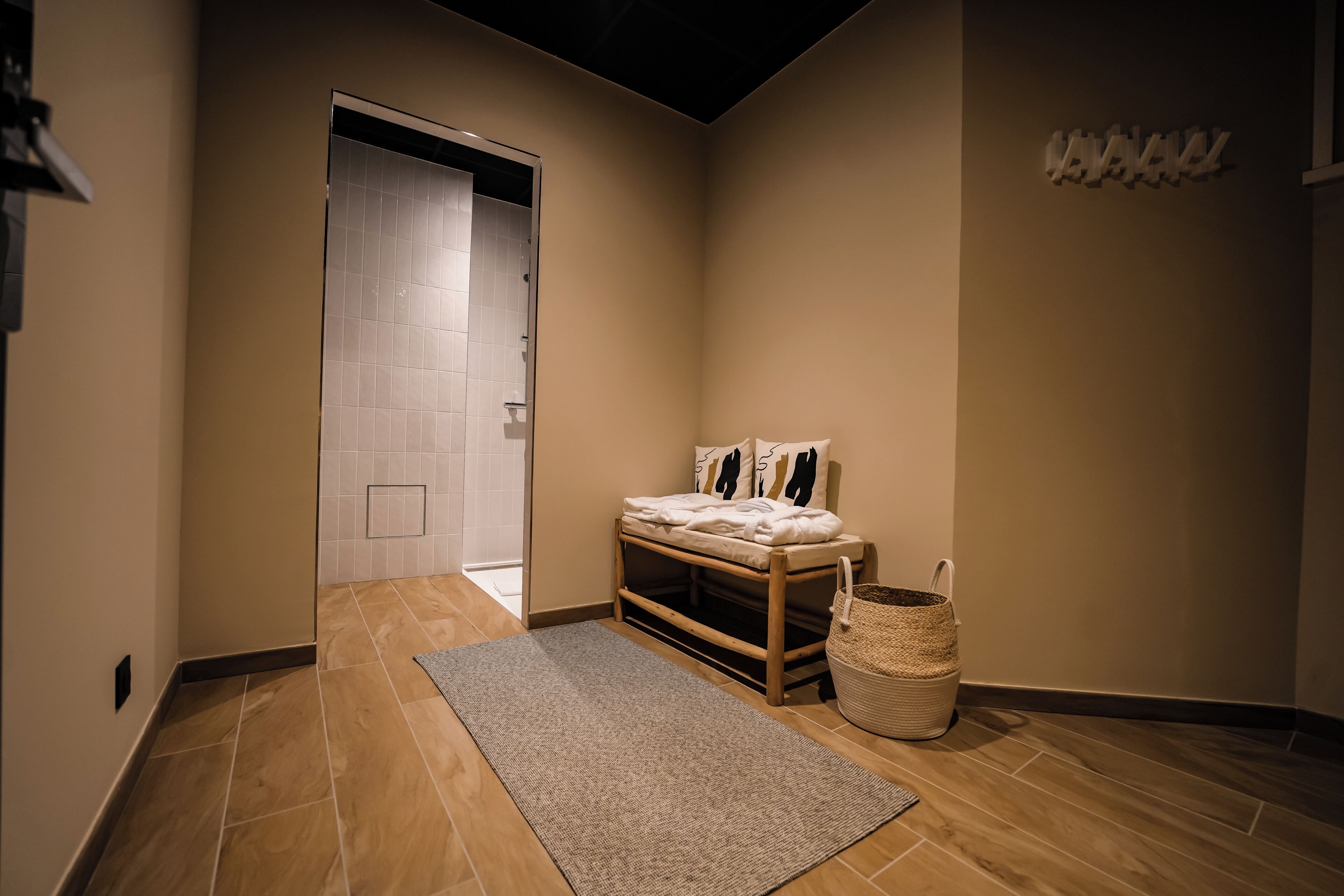 Un pasillo con piso de madera, un tapete, un banco con almohadas y una cesta tejida.