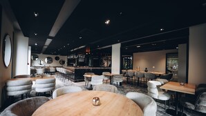 A modern bar area with round tables and cushioned chairs, a bar counter with bottles, and a seating area with a carpeted floor. - Les Lodges de Socrate (Le Vaudreuil)
