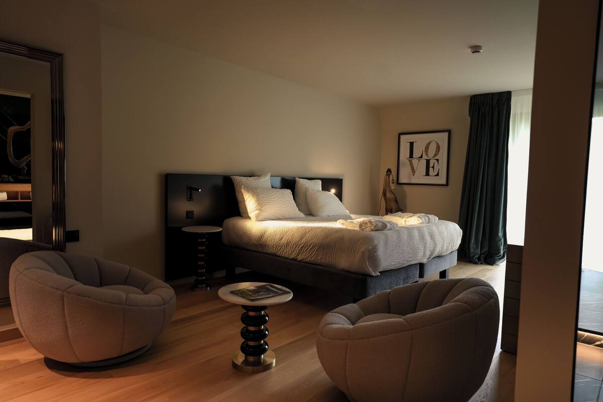 Ein modernes Hotelzimmer mit einem Bett, zwei Sesseln, einem kleinen runden Tisch und einem gerahmten Kunstwerk an der Wand.