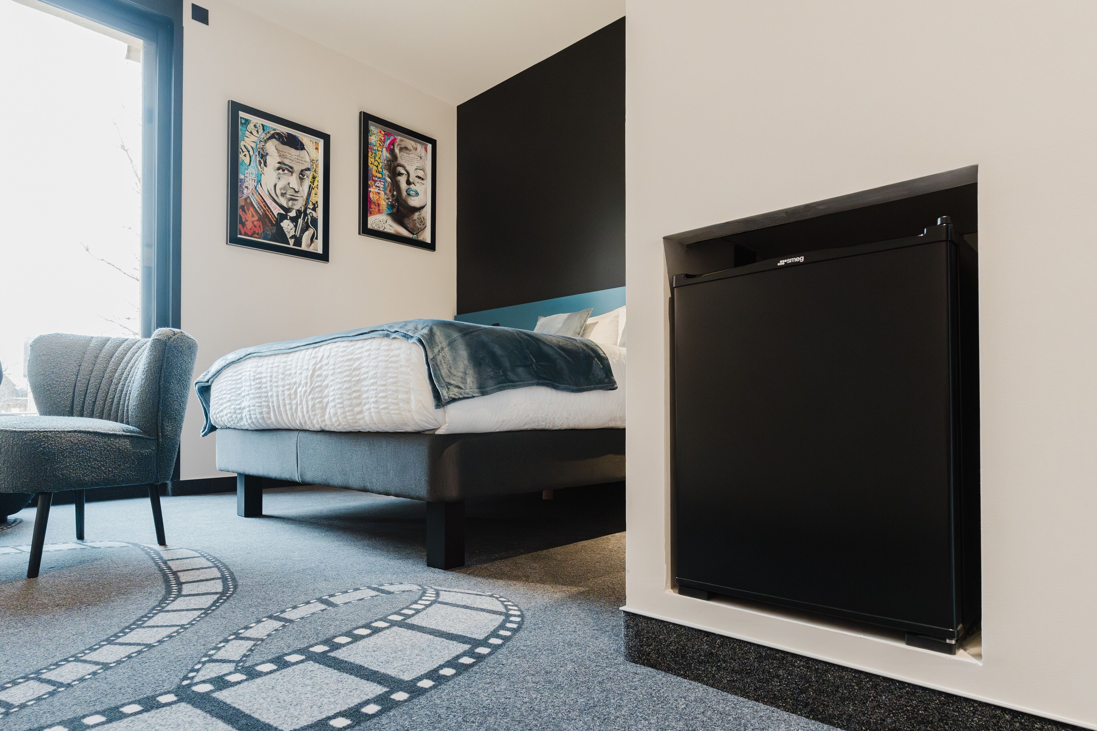 A modern bedroom with a bed, a chair, and a large black screen on the wall.