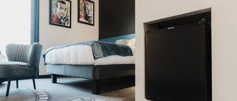A modern bedroom with a bed, a chair, and a large black screen on the wall.