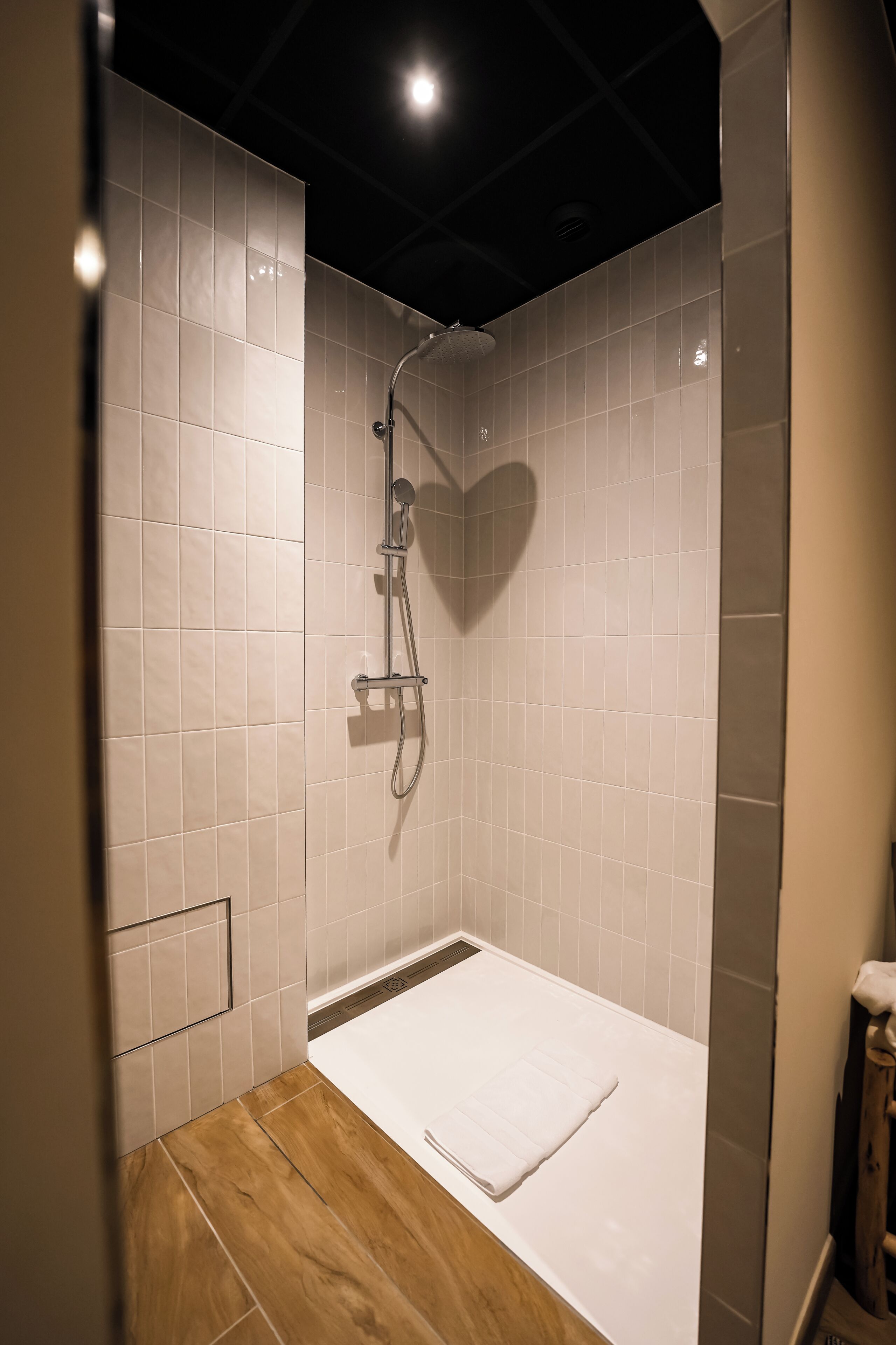 Een moderne douche met een hartvormige schaduw op de muur, een houten vloer en een witte handdoek op de grond.