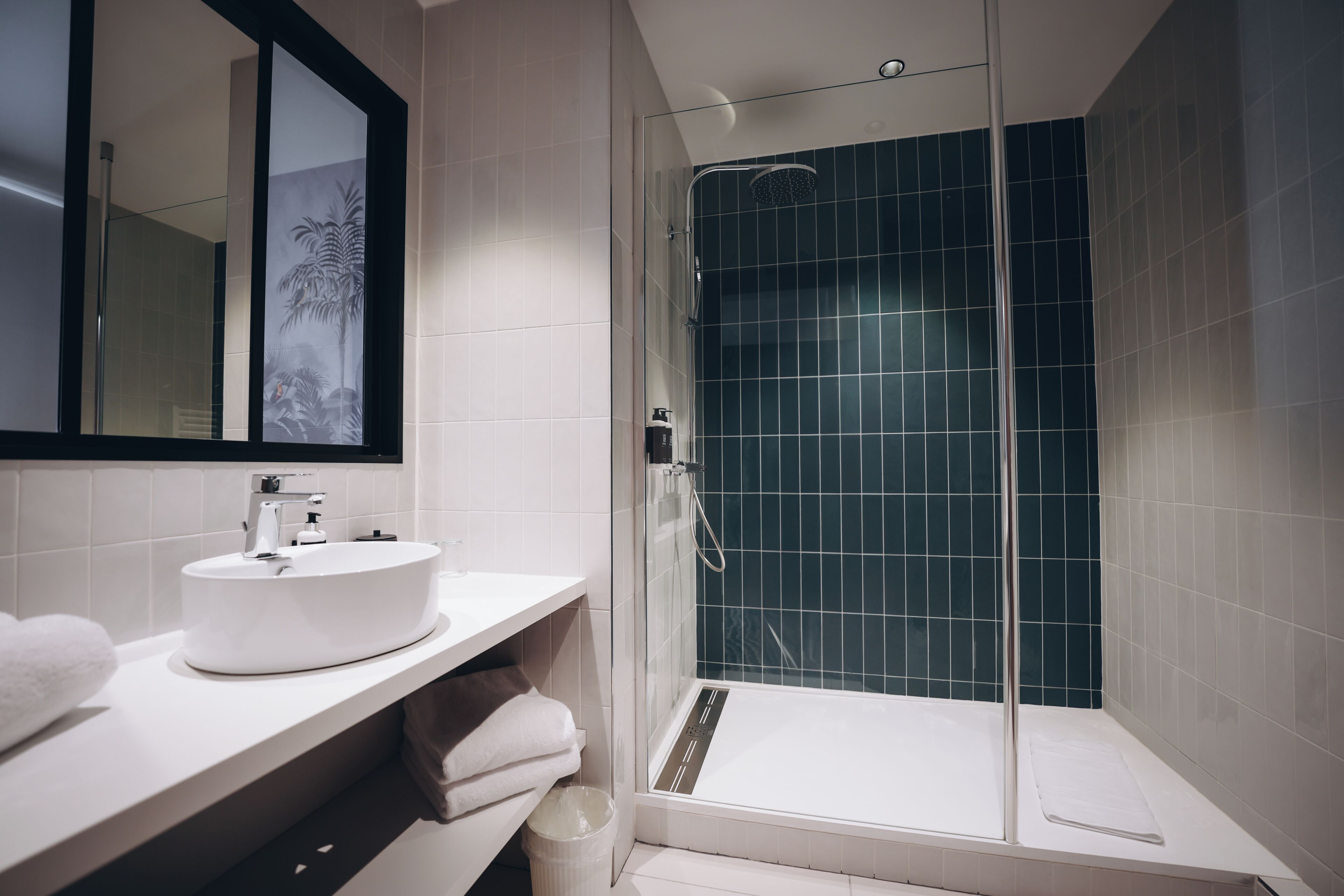A modern bathroom with a glass-enclosed shower, a white sink, and a mirror with a decorative frame.