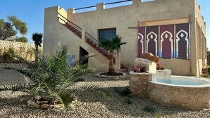 A building with a stone staircase, a small pool, and a garden with palm trees.