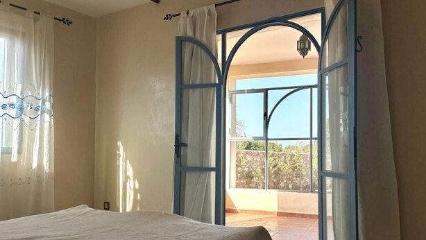 A bedroom with a bed, a balcony with a view, and a door with a curtain.