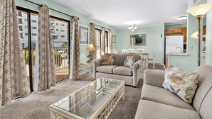 A living room with a sofa, a glass coffee table, and a dining area with a table and chairs. - B110 at the Myrtle Beach Resort (Myrtle Beach)