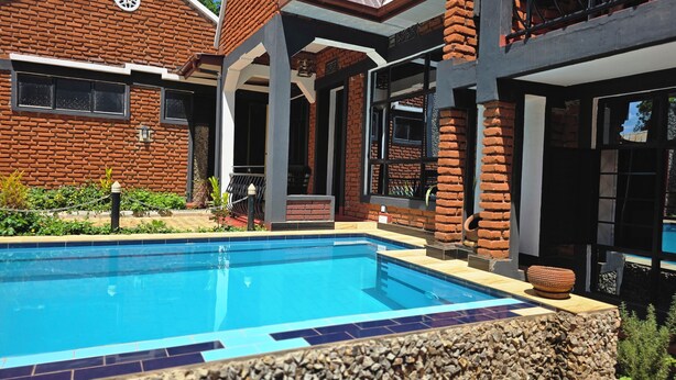 Una piscina con borde de azulejos, rodeada por un muro de ladrillo y una zona de patio techada.
