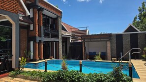 A modern building with a swimming pool, a covered outdoor seating area, and a stone wall. - Unique Homestays A - 2 bedrooms with swimming pool and Free Wi-Fi (Arusha)