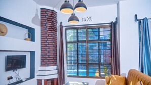 Una sala de estar con chimenea de ladrillo, un sofá, una mesa de centro con revistas y un televisor montado en la pared.