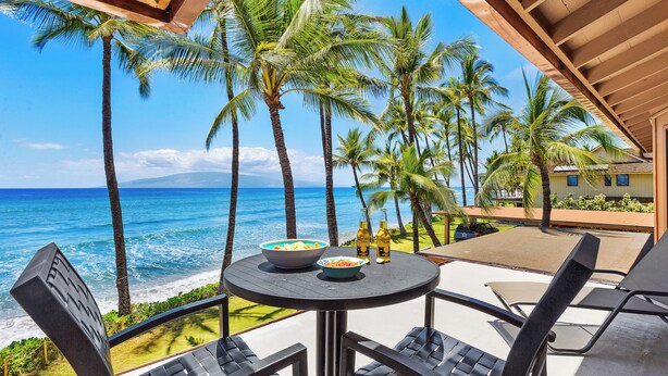 A table with two bowls and two bottles, overlooking a beach with palm trees and the ocean.