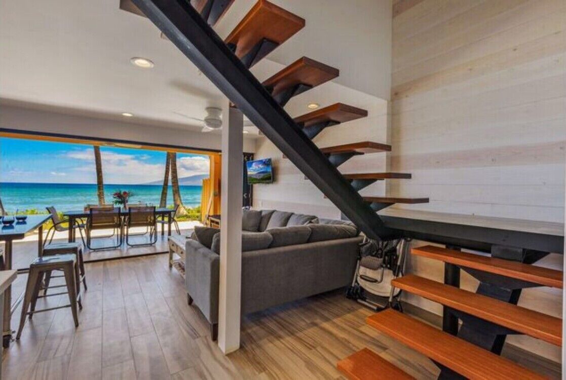A modern interior with a staircase, a sofa, and a dining area with a view of the ocean.