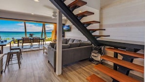 A modern interior with a staircase, a sofa, and a dining area with a view of the ocean.
