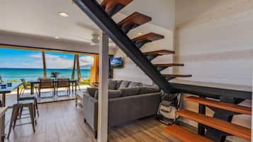 A modern interior with a staircase, a sofa, and a dining area with a view of the ocean.