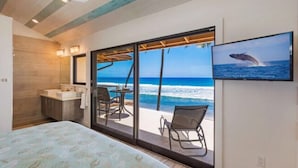 A bedroom with a bed, a bathroom, and a large sliding glass door leading to a balcony with a view of the ocean.
