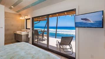A bedroom with a bed, a bathroom, and a large sliding glass door leading to a balcony with a view of the ocean.