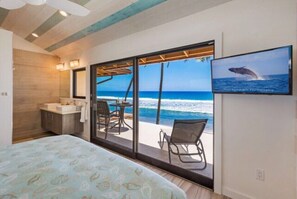 A bedroom with a bed, a bathroom, and a large sliding glass door leading to a balcony with a view of the ocean.
