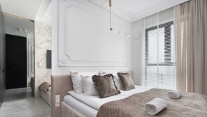A modern bedroom with a large bed, a walk-in closet, and a bathroom with a glass shower. - Chronos - Warszawa Wola by Downtown Apartments (Warsaw)