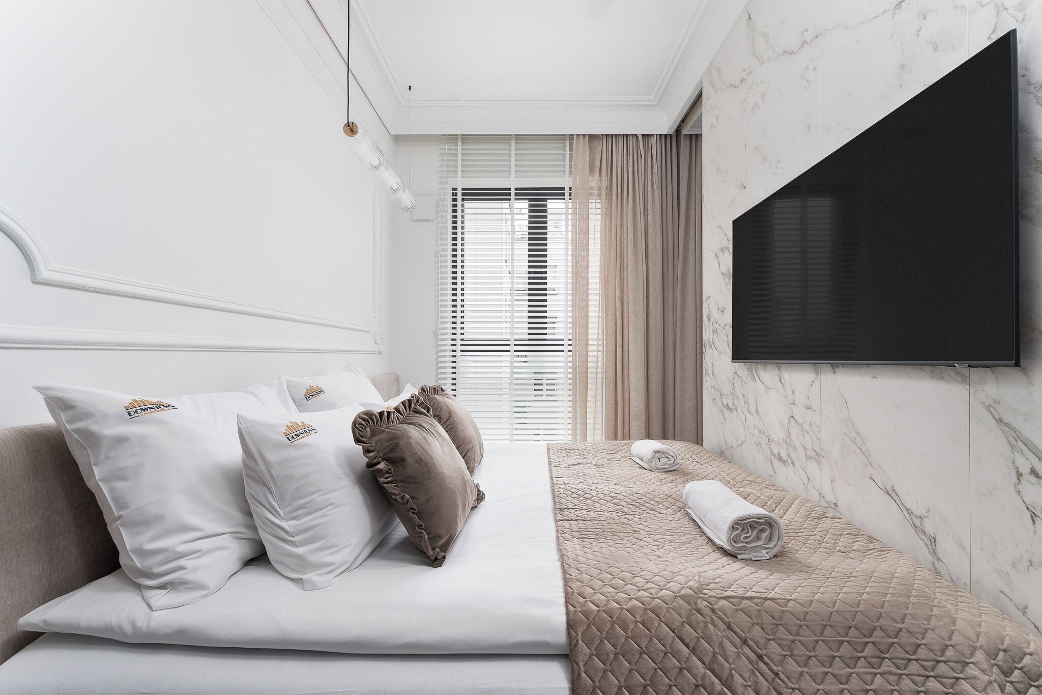 A modern bedroom with a bed, pillows, a TV, and a window with blinds.