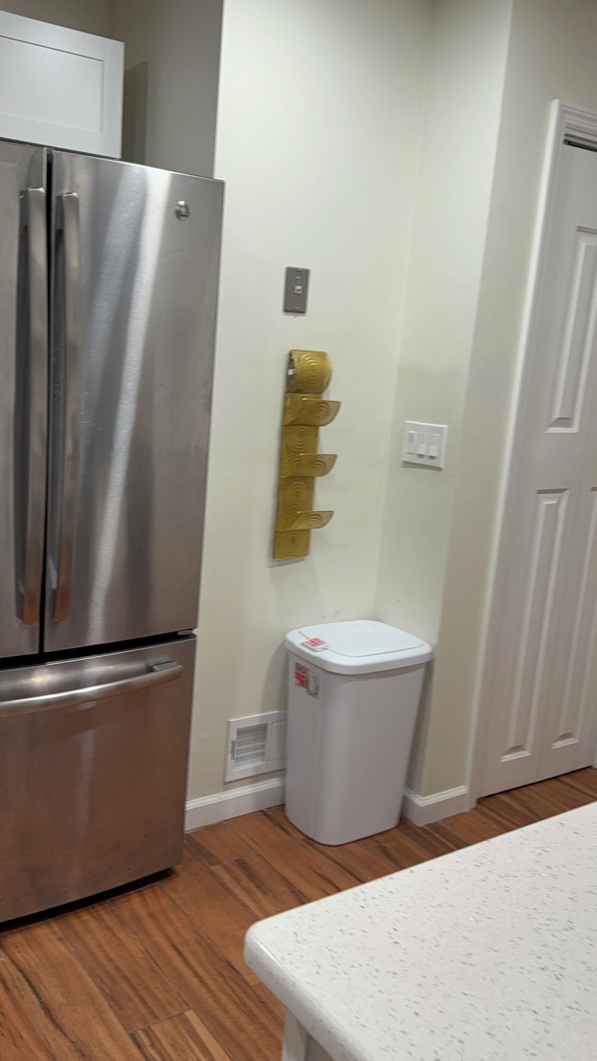 A kitchen with a stainless steel refrigerator, a trash bin, and a white countertop.
