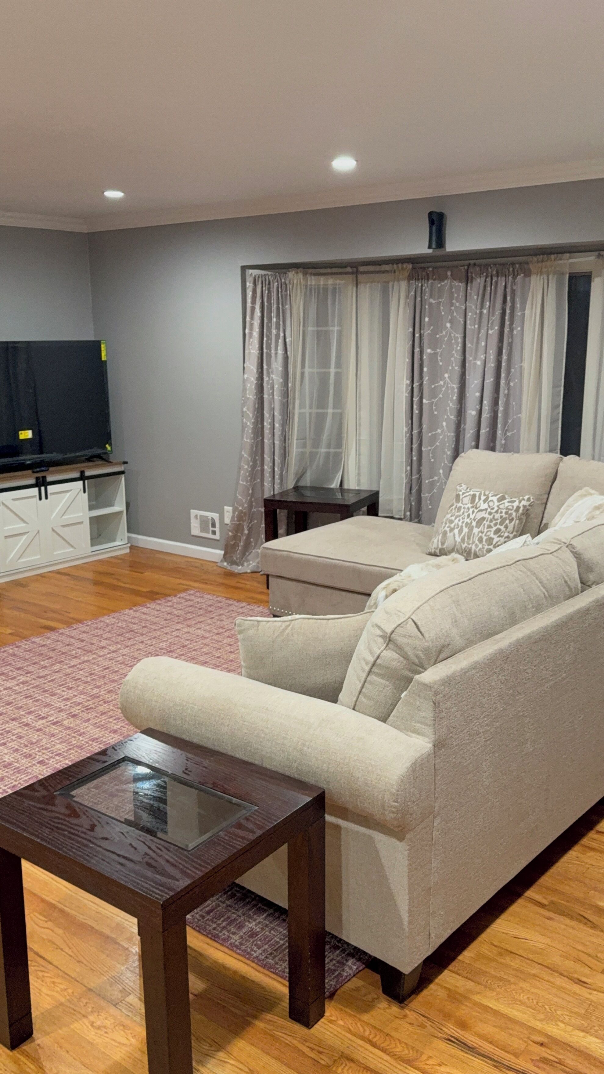 Una sala de estar con un sofá, una mesa de centro, un televisor sobre un mueble bajo y una ventana con cortinas.