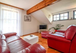 Una sala de estar con un sofá de cuero rojo, una mesa de centro blanca, un televisor y una viga de techo de madera.