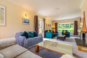 A cozy living room with a fireplace, two sofas, a coffee table, and a large window with curtains. - Host & Stay | Alderfen View (Norwich)