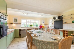 Une cuisine avec une table à manger pour quatre personnes, des meubles de couleur verte et une fenêtre donnant sur un paysage verdoyant.