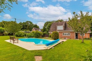 A backyard with a swimming pool, a bench, and a house with a brick exterior. - Host & Stay | Alderfen View (Norwich)