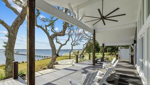 A covered deck with white Adirondack chairs, a wooden floor, and a view of the water.