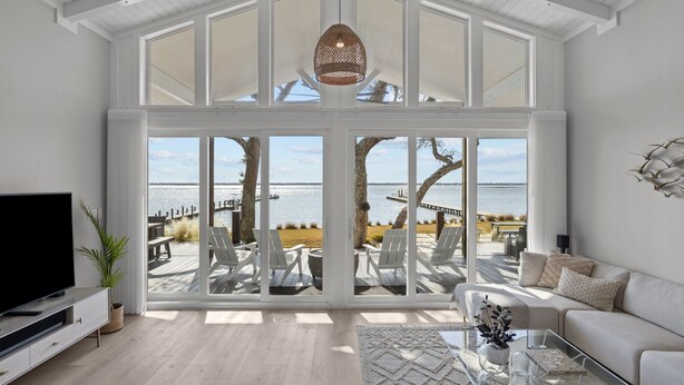 A spacious living room with a large bay window overlooking a deck and the sea.