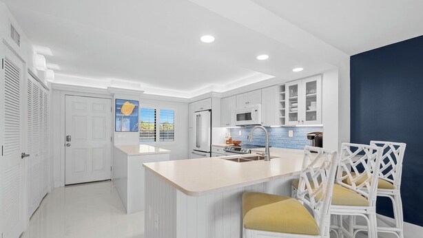 A modern kitchen with white cabinetry, a central island with a sink, and two wicker chairs with yellow cushions.