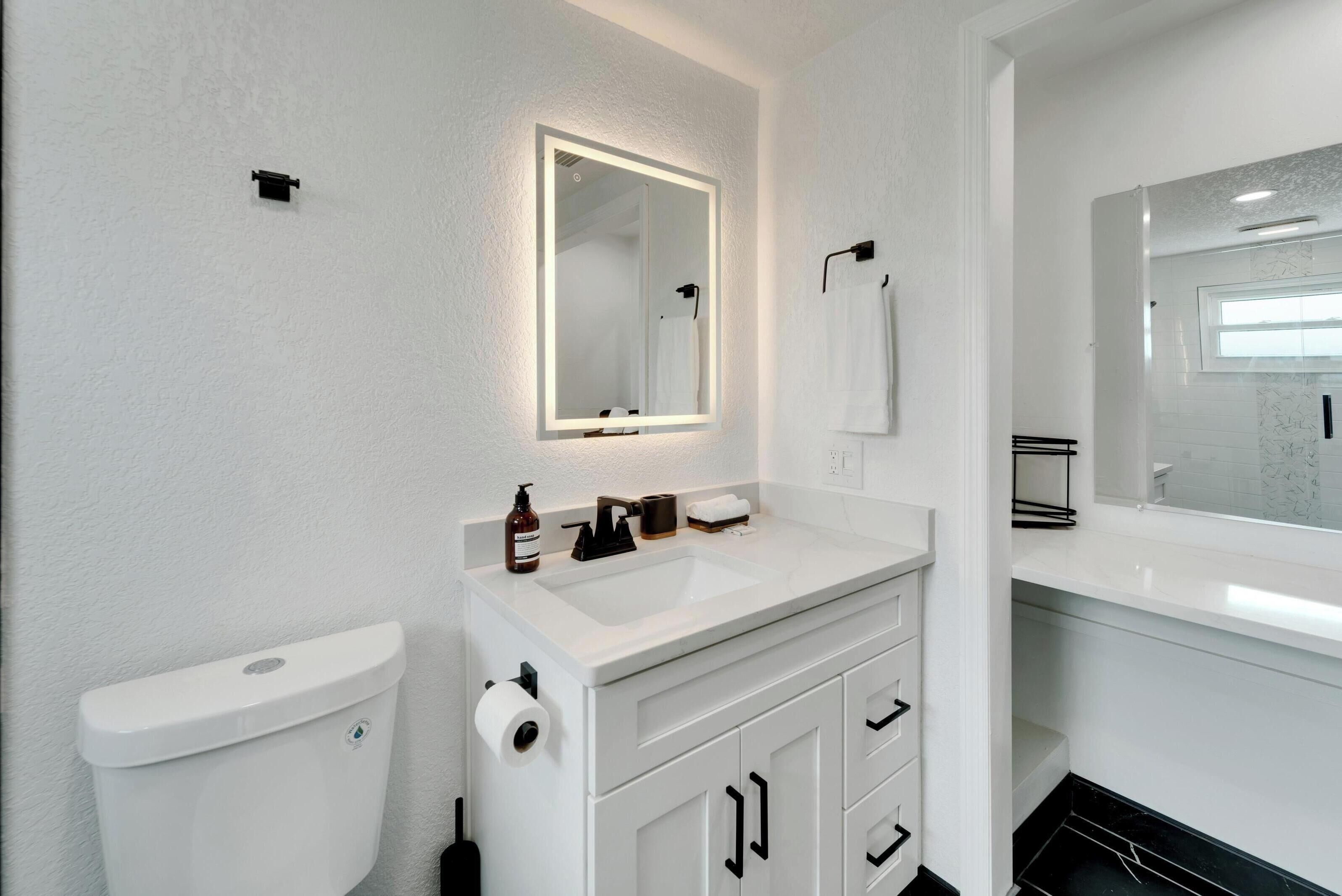 Un baño moderno con un lavabo blanco, un inodoro y un espejo grande.