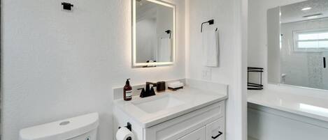 Un baño moderno con un lavabo blanco, un inodoro y un espejo grande.
