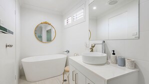 Une salle de bain moderne avec une baignoire sur pieds, un lavabo rond et un miroir doté d’un cadre doré.