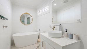 Een moderne badkamer met een vrijstaand bad, een rond wastafeltje en een spiegel met een gouden lijst.