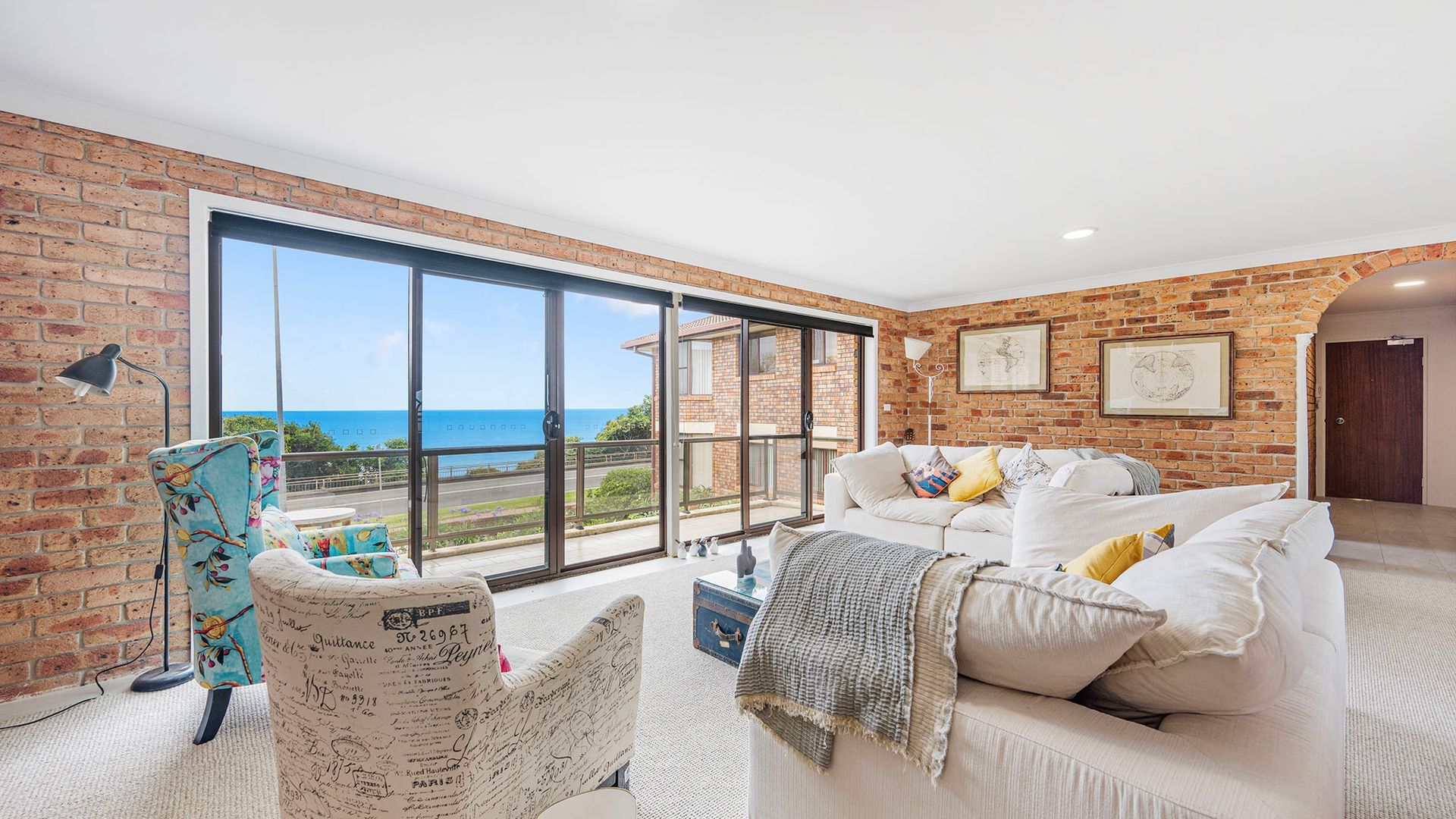 A room with a large sliding glass door leading to a balcony with a view of the sea.