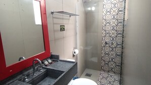 A bathroom with a red-framed mirror, a sink with a faucet, a toilet, and a shower area with patterned tiles. - HOTEL MONTE CASTELO LTDA. (Rio de Janeiro)