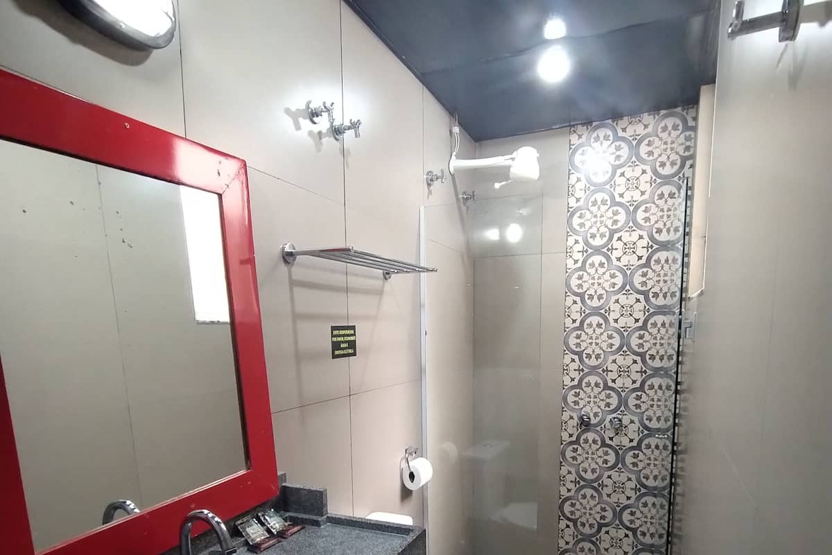 Une salle de bain avec un miroir à cadre rouge, un lavabo avec un robinet, des toilettes et un espace douche avec des carreaux à motifs.