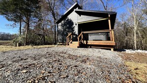 Eine Holzhütte mit einer Holzterrasse und einer überdachten Veranda, umgeben von Bäumen und Kiesgrundstück.